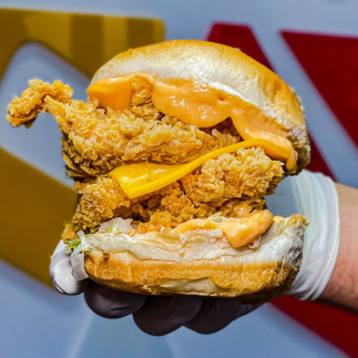 a gloved hand holding a burger that is packed with two layers of fried chicken and cheese.
